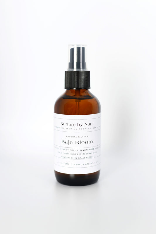 Brown spray bottle labeled 'Nurture by Nuri Baja Bloom' on a white background. Room and linen Spray