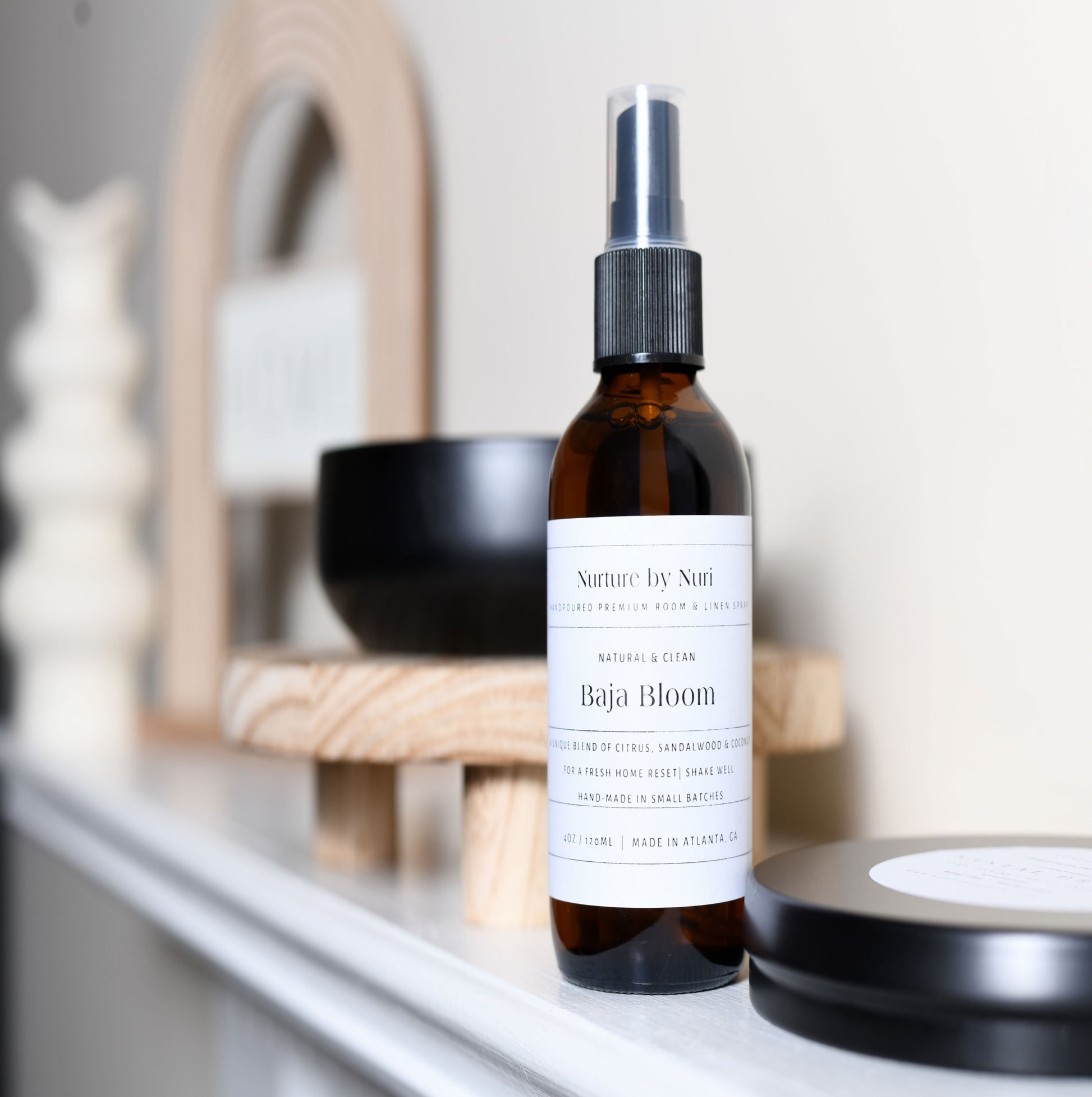 Bottle of 'Baja Bloom' room spray on a shelf with decorative items in the background