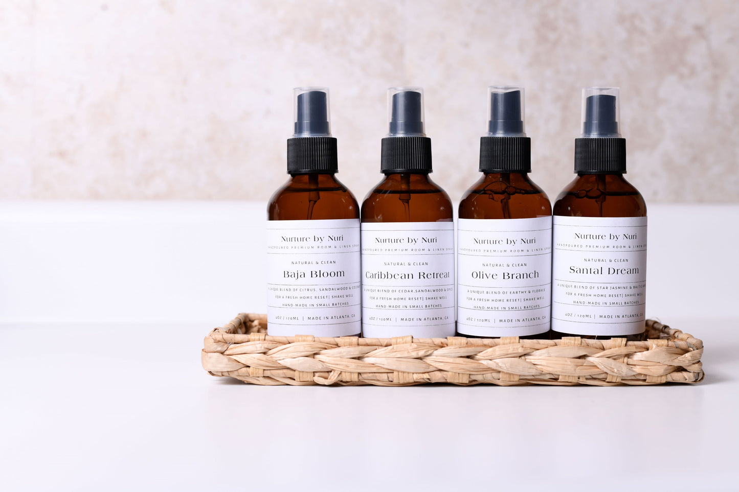 Five brown Nurture by Nuri room and linen spray bottles with labels on a woven tray against a light background